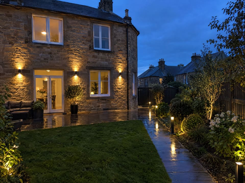 Garden wall lights and path lights on a stone house at dusk