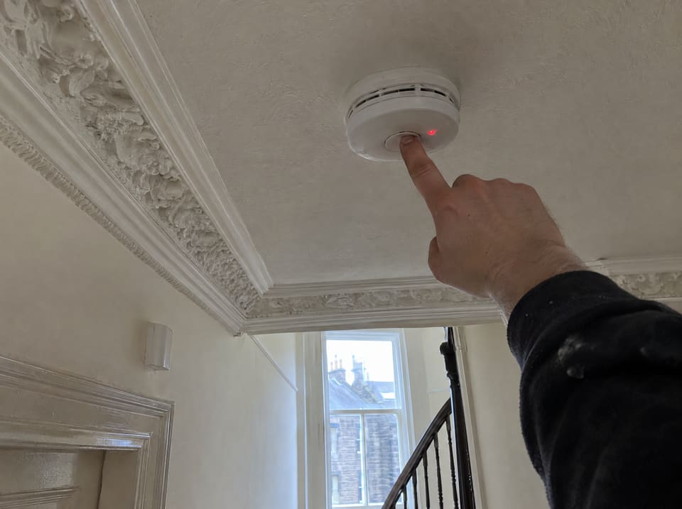 Testing a mains smoke alarm on a tenement hallway ceiling